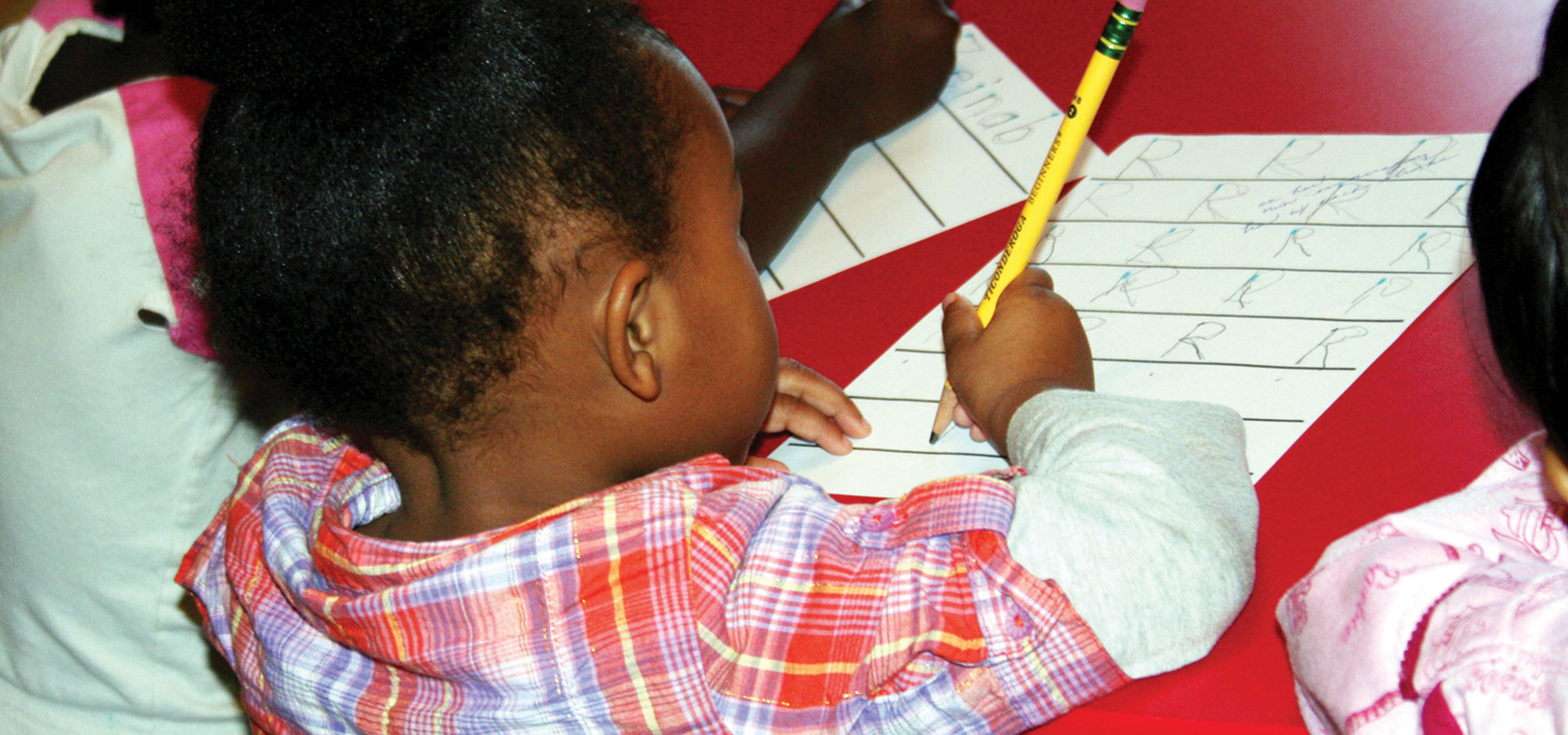 A young girl practicing writing with guidance during a learning activity at Phoenix Family