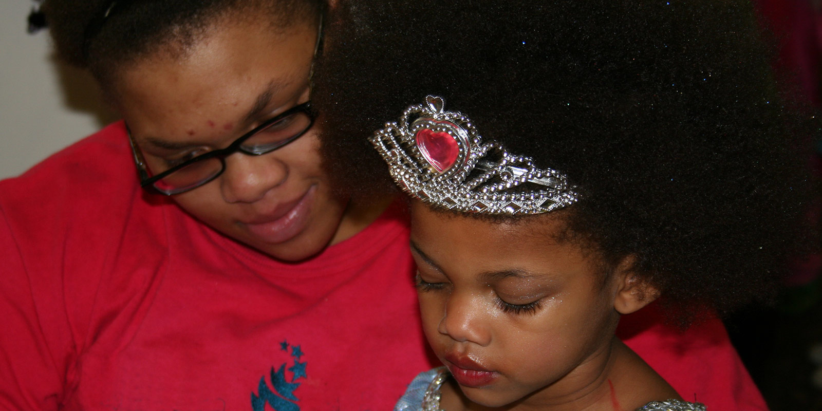 A mother sitting with her young daughter wearing a tiara during a quiet moment together in their apartment community